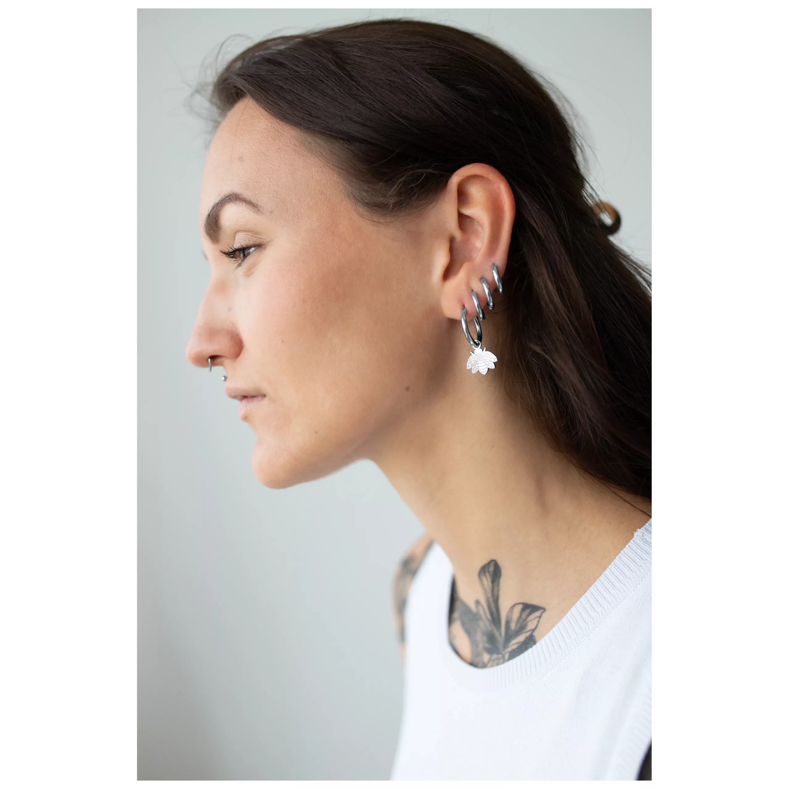Frau mit silbernen Little Bee Hoops Ohrringen vor neutralem Hintergrund