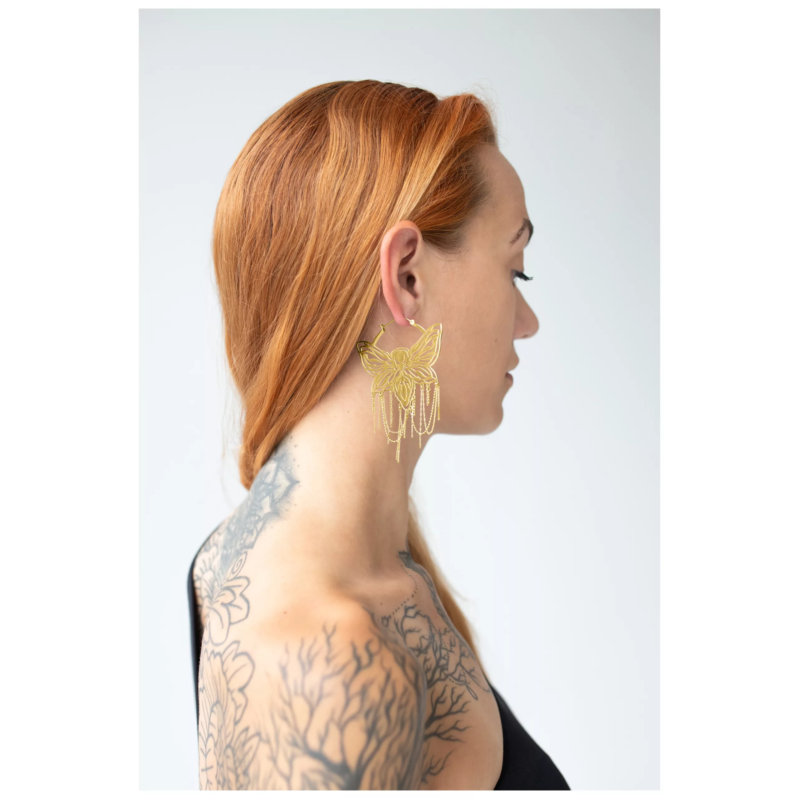 Frau mit goldenen Moth Chain Hoops Ohrringen vor hellem Hintergrund