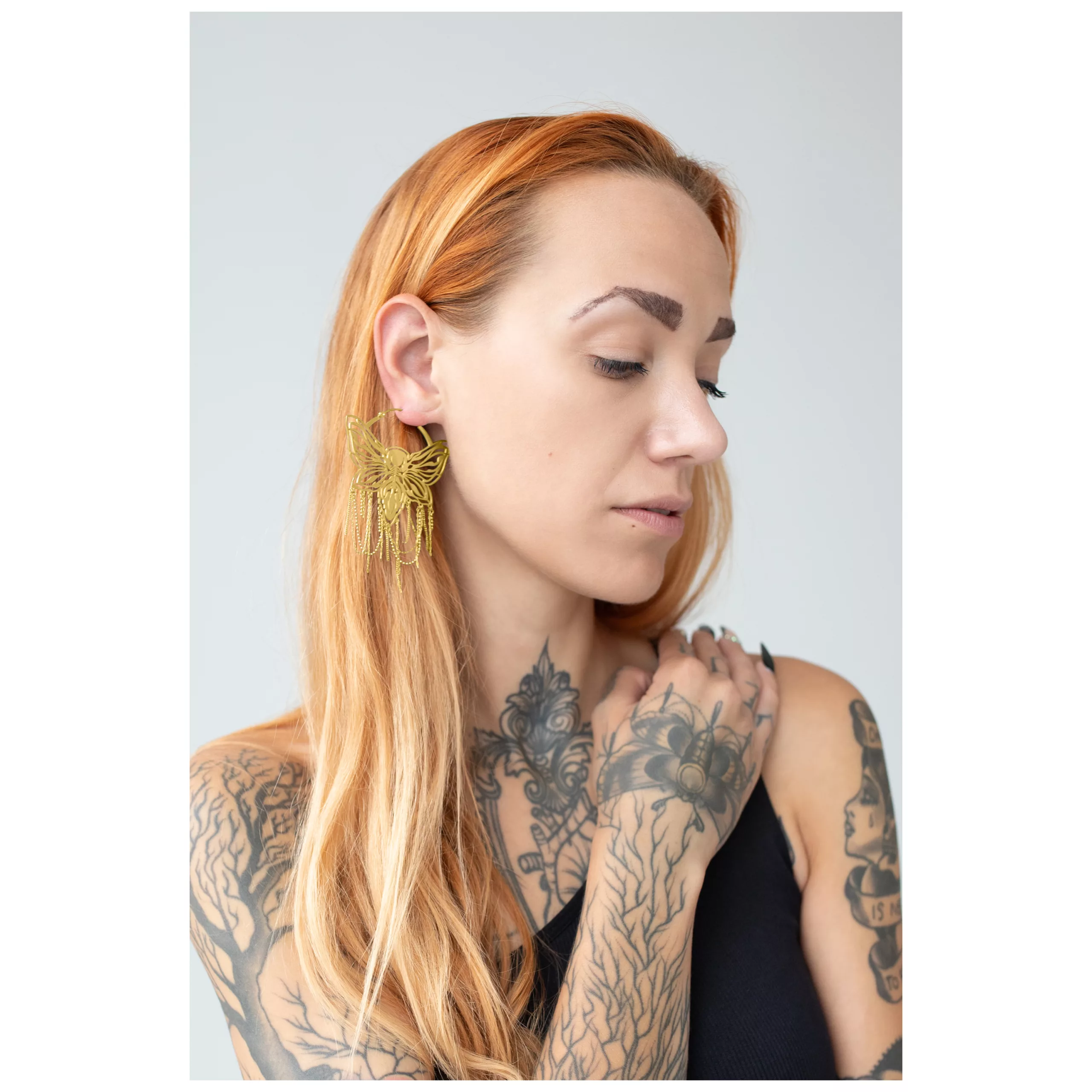 Frau mit goldenen Moth Chain Hoops Ohrringen vor neutralem Hintergrund