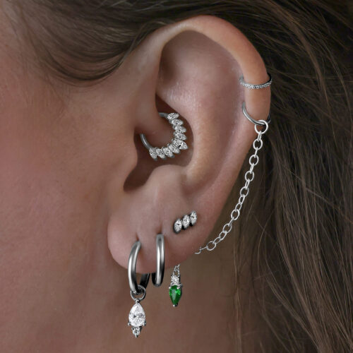 Mehrere Ohrringe im Ohr, darunter schwarze Little Tear Hoops mit grünem Kristall.
